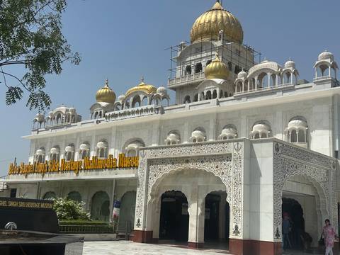       A white gurdwara with golden domes and intricate carvings.
  