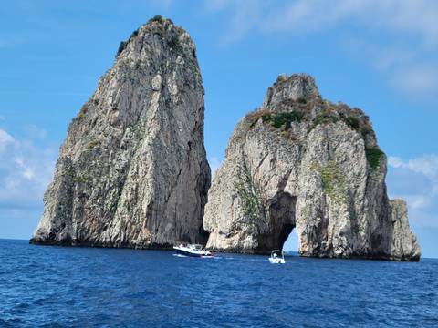 Two large rocky cliffs rising from the sea with boats nearby.