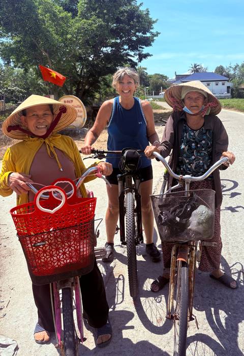       Three local women with baskets posing with a tourist in the middle.
  