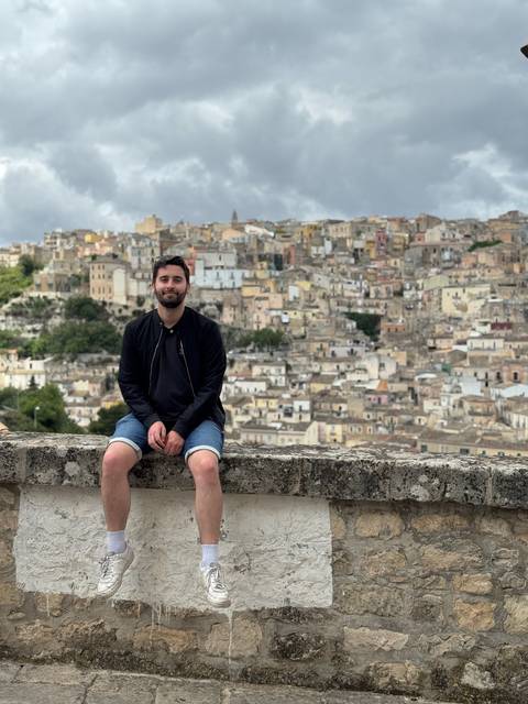 Person posing with a charming hillside town in the background.