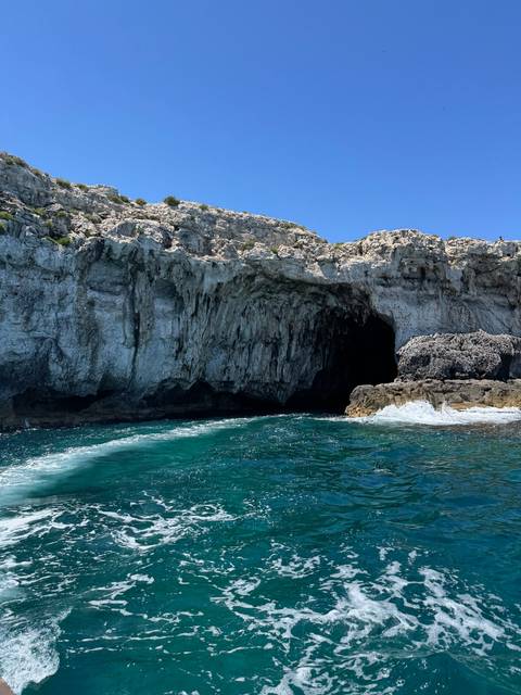 Seaside cliffs with a rocky cave and clear blue water.