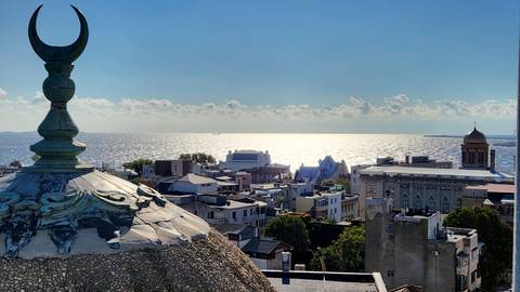 Elevated view of a coastal cityscape with the sea reflecting sunlight in the distance.