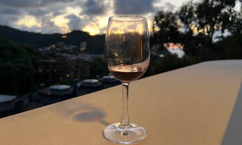 A glass of wine in the foreground with a scenic view at sunset.