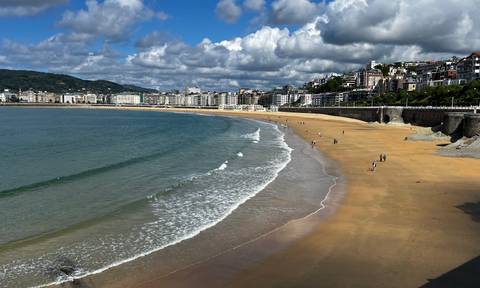 An expansive sandy beach with city buildings on a sunny day.
