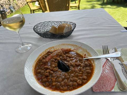 A dish of beans and seafood with a glass of wine.