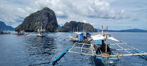       Traditional boats on a calm sea near dramatic cliffs.
  