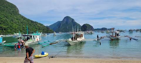       Traditional outrigger boats docked in a bay with cliffs.
  