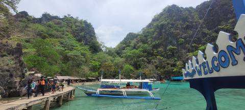       Dock with boats near tall, rocky cliffs and green water.
  