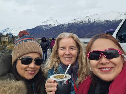 Three women smiling at the camera with snowy mountains in the background.