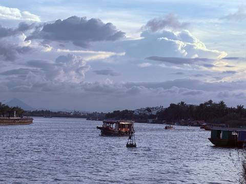       Boats on a river at dusk with a cloudy sky.
  