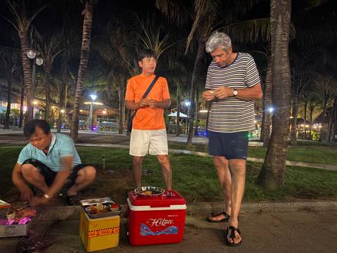       Three people having a picnic near palm trees, with string lights visible.
  