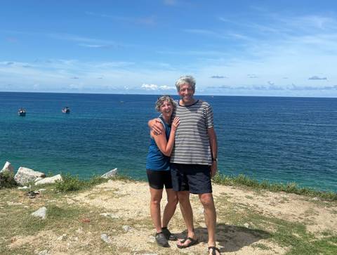       Couple at the seaside smiling at the camera with a blue ocean backdrop.
  