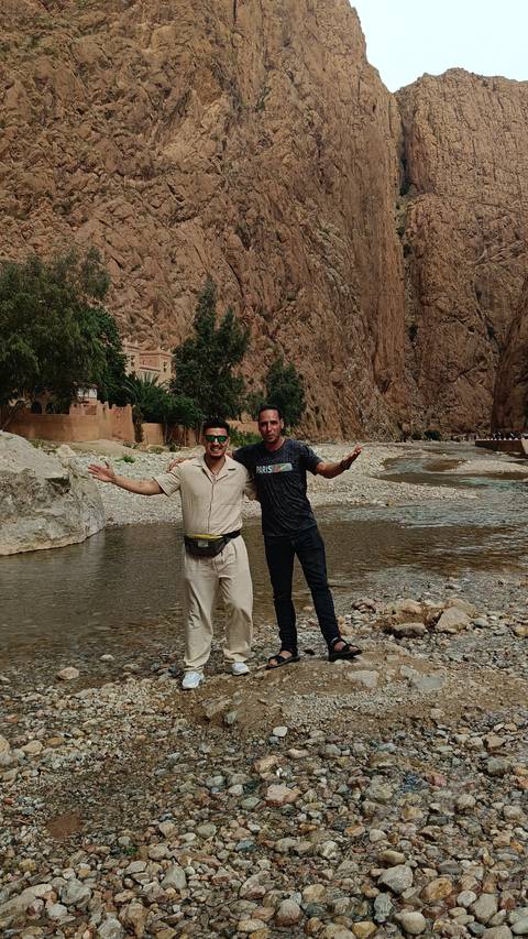       Two men posing by a river with rocky cliffs.
  