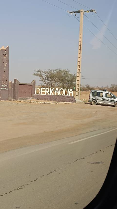       A sign that reads 'DERKAOUI' by a roadside in a desert area.
  