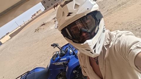       A person wearing a helmet posing with a quad bike in the desert.
  