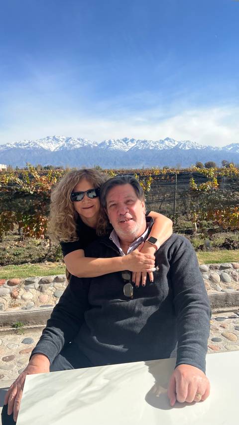 A couple posing in front of a vineyard with mountains in the background.