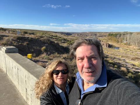 A couple taking a selfie on a bridge with a scenic landscape.