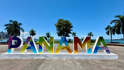       Colorful 'Panama' sign with palm trees and cityscape in the background.
  