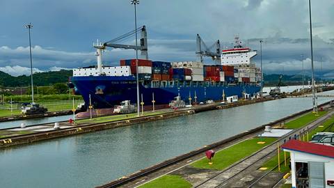       Large container ship passing through a canal under a cloudy sky.
  