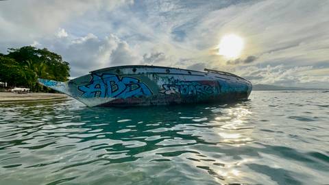      Graffiti covered boat in water with a setting sun.
  