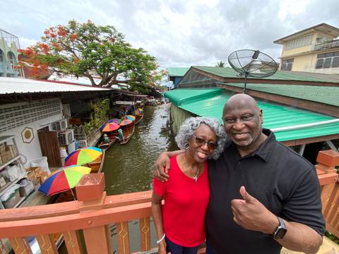 Couple posing with vibrant market and boats.