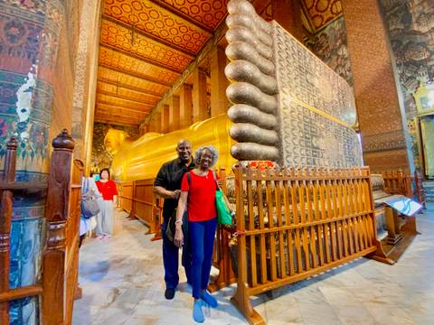       Two people posing in front of a large golden reclining Buddha.
  