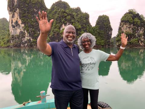 Two people waving in front of a scenic bay with limestone karsts.