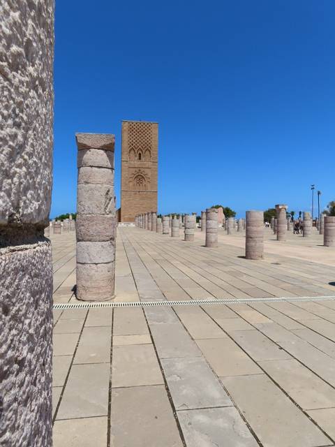 Ruins of stone columns and a tall tower under a clear blue sky.