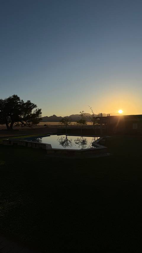       Sunset over a swimming pool with mountains in the background.
  
