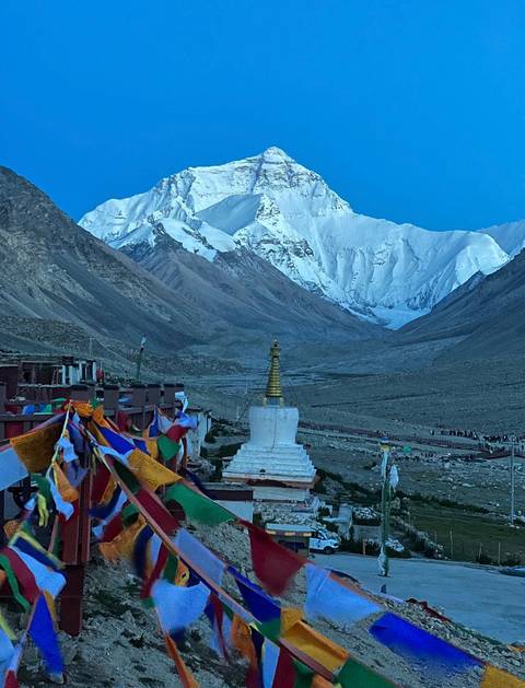Snow-capped mountain with a stupa and prayer flags in the foreground.