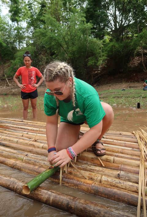       A person tying bamboo sticks on a raft.
  