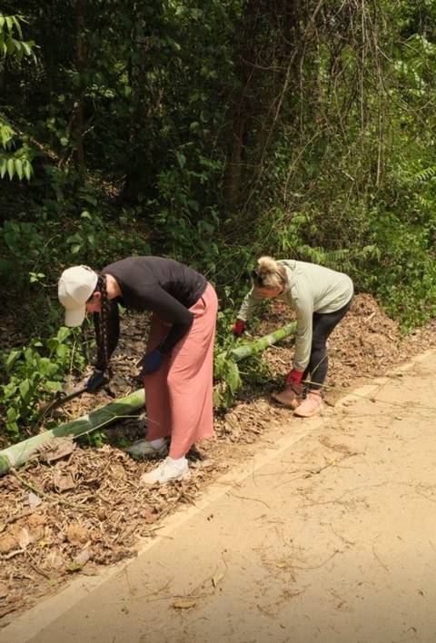       Two people clearing brush along a dirt path.
  