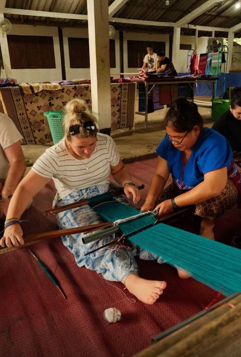 Two people working together on a loom, weaving fabric.