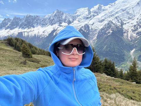 Person in blue attire posing with snow-capped mountains in the background.