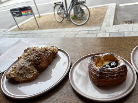       Two pastries on plates by a window with a view of a bike.
  