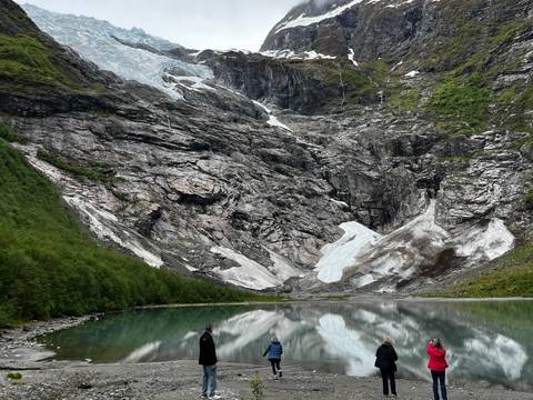       People standing by a glacial lake with glacier in the background.
  