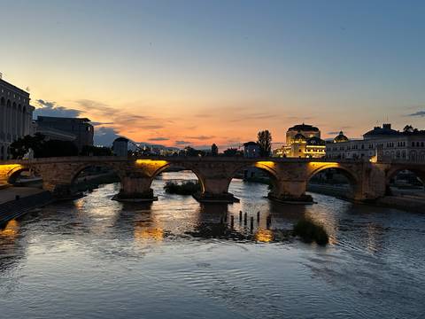 Historic stone bridge over a calm river at sunset.