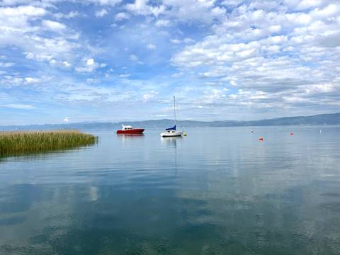 Tranquil lake with boats and mountains in the distance.