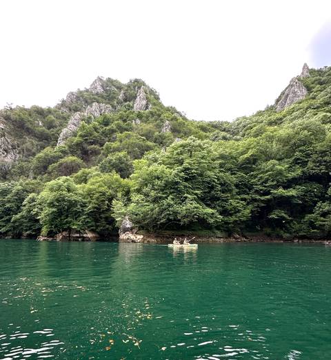 Kayakers in clear green water surrounded by forested cliffs.