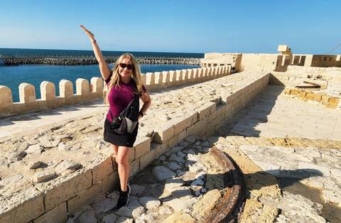 Smiling woman posing on historic stone walls with sea view.