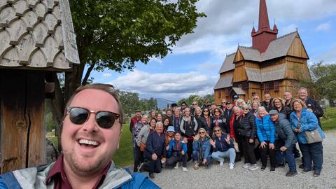       A group of tourists posing in front of a wooden church.
  