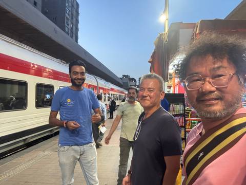       Men posing at a train station with a train visible in the background.
  