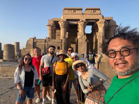       Group of people posing in front of historic Egyptian ruins at sunset.
  