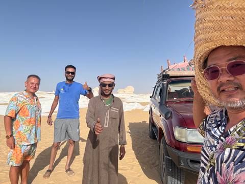       Group of people posing in a desert landscape with a vehicle.
  