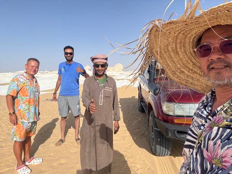       Group of people posing in a desert landscape with a vehicle.
  