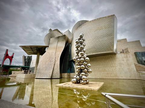       The Guggenheim Museum in Bilbao with reflective sculptures outside.
  