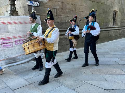       Parade with men in traditional outfits playing drums and bagpipes.
  