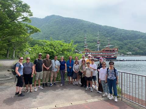 Large group of people posing by a lakeside with mountainous background.