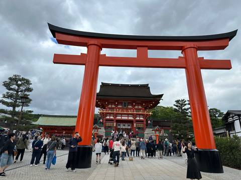 People walking under a large red torii gate at a temple complex.