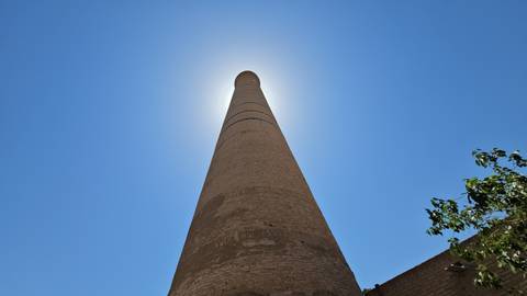       Tall narrow minaret with a bright sun forming a halo effect at the top.
  